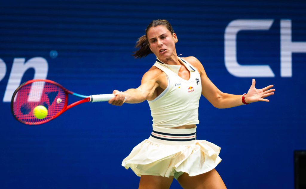 Emma Navarro, in white sleeveless shirt and skirt, hits a shot aainst Coco Gauff at the US Open