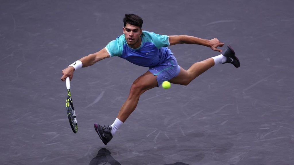 Carlos Alcaraz of Spain, in blue shirt and shorts, rushes to return the serve at the 2024 Rolex Paris Masters on Tuesday. Alcaraz reaches Paris Masters third round